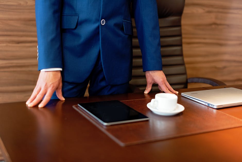 Professional businessman in blue suit standing by a desk with a tablet and coffee cup