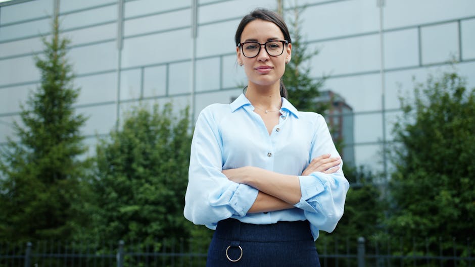 Confident businesswoman standing with arms crossed, wearing glasses, outside office building